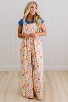 Woman wearing a floral jumpsuit with a blue top against a white paneled wall.