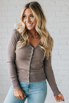 Woman wearing a brown cardigan and blue jeans against a white brick wall.