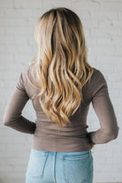 Person wearing a brown long-sleeve top and light blue jeans with a white brick wall background