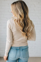 Person wearing a beige sweater and blue jeans against a white brick wall.