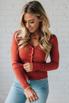 Woman wearing a red cardigan and blue jeans against a white brick wall.