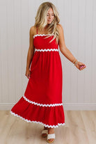 Woman wearing a red dress with white trim against a white wall.