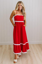 Woman wearing a red dress with white trim against a white wall.