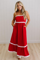 Woman wearing a red dress with white trim against a white wall.