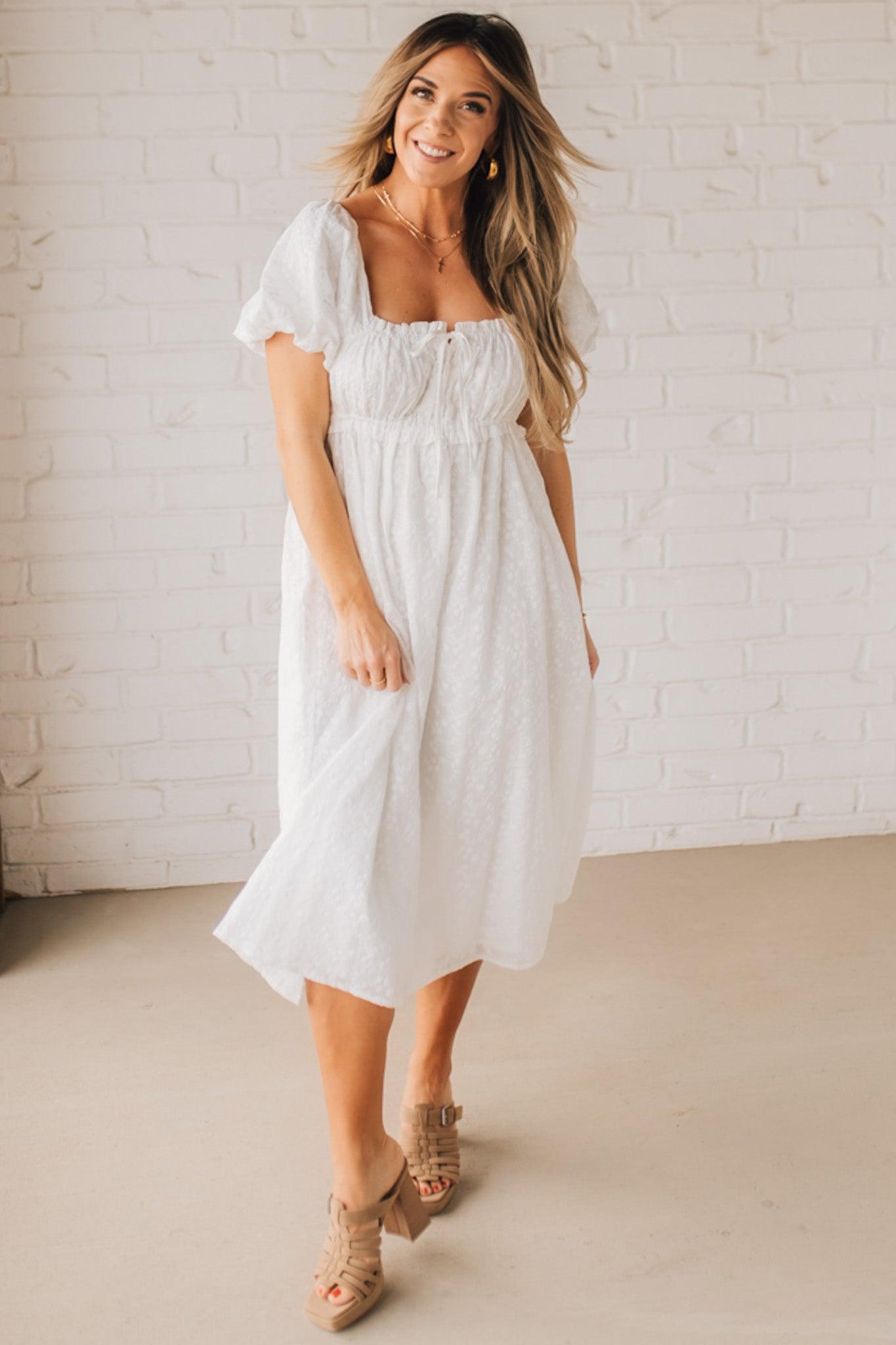 BLONDE WOMAN WEARING A WHITE, PUFF HALF SLEEVE, SQUARE NECKLINE, EYELET MIDI DRESS WITH TIE STRAP BACK.