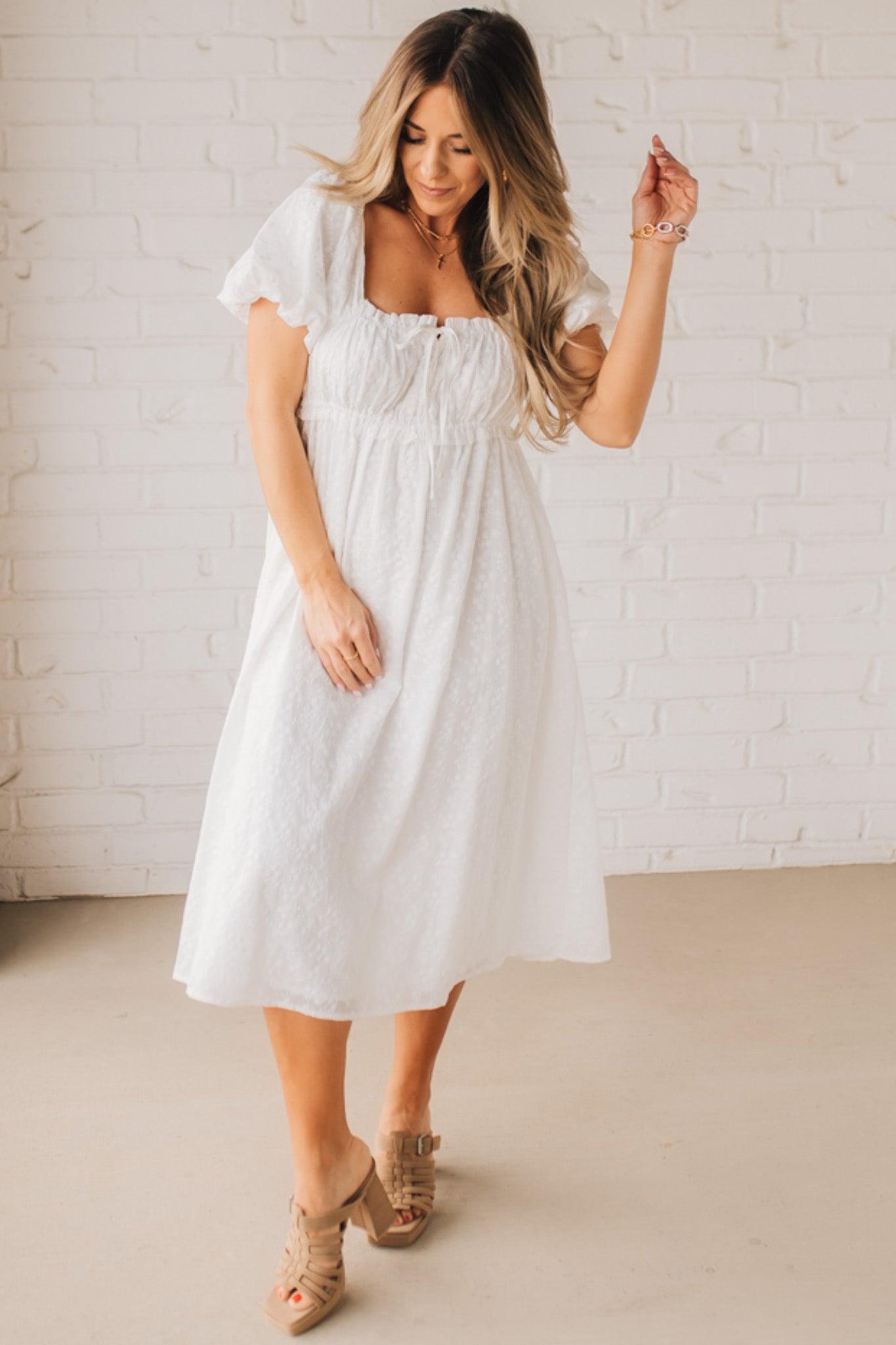 BLONDE WOMAN WEARING A WHITE, PUFF HALF SLEEVE, SQUARE NECKLINE, EYELET MIDI DRESS WITH TIE STRAP BACK.