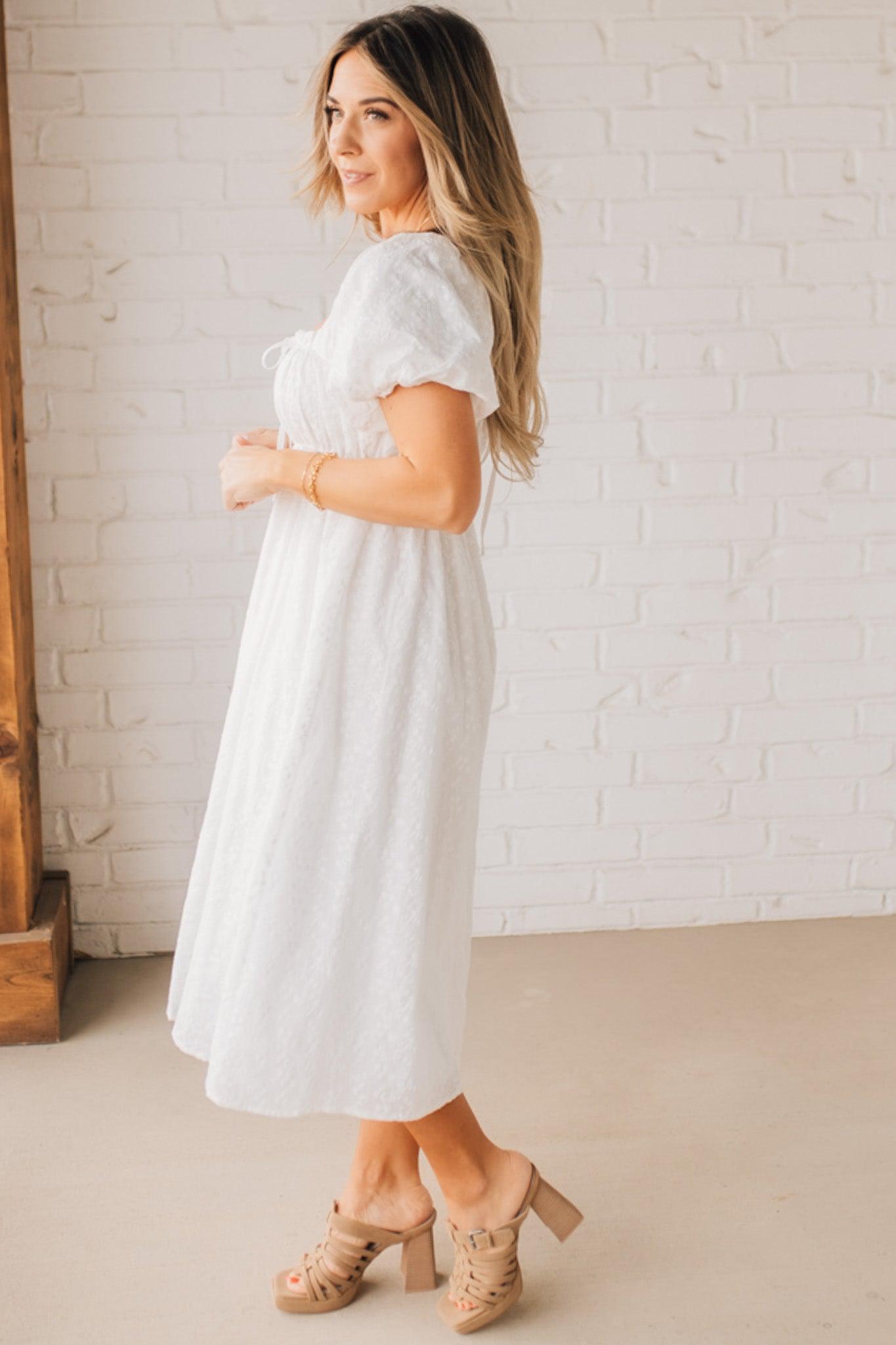 BLONDE WOMAN WEARING A WHITE, PUFF HALF SLEEVE, SQUARE NECKLINE, EYELET MIDI DRESS WITH TIE STRAP BACK.