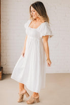 BLONDE WOMAN WEARING A WHITE, PUFF HALF SLEEVE, SQUARE NECKLINE, EYELET MIDI DRESS WITH TIE STRAP BACK.