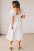 BLONDE WOMAN WEARING A WHITE, PUFF HALF SLEEVE, SQUARE NECKLINE, EYELET MIDI DRESS WITH TIE STRAP BACK.