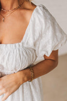 BLONDE WOMAN WEARING A WHITE, PUFF HALF SLEEVE, SQUARE NECKLINE, EYELET MIDI DRESS WITH TIE STRAP BACK.