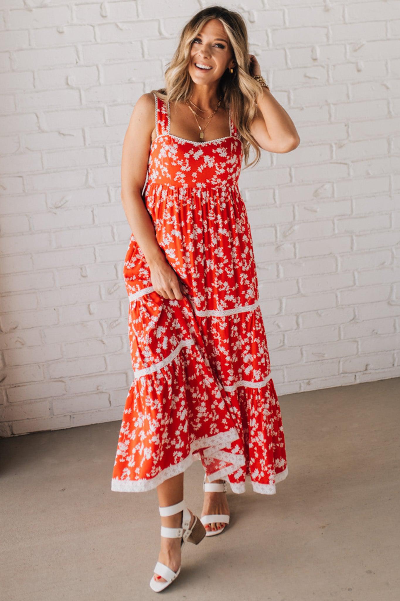 BLONDE WOMAN WEARING A RED FLORAL PRINT SLEEVELESS MAXI FEATURES: TIERED SKIRT PANEL WITH LACE INSET DETAIL, SMOCKED BACK, HIDDEN SIDE ZIPPER, THICK STRAPS WITH SCALLOPED LACE EDGES, SIDE POCKETS AND FULL LINING.