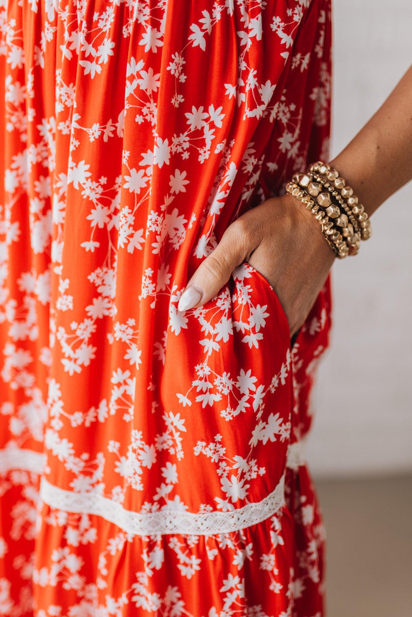 BLONDE WOMAN WEARING A RED FLORAL PRINT SLEEVELESS MAXI FEATURES: TIERED SKIRT PANEL WITH LACE INSET DETAIL, SMOCKED BACK, HIDDEN SIDE ZIPPER, THICK STRAPS WITH SCALLOPED LACE EDGES, SIDE POCKETS AND FULL LINING.