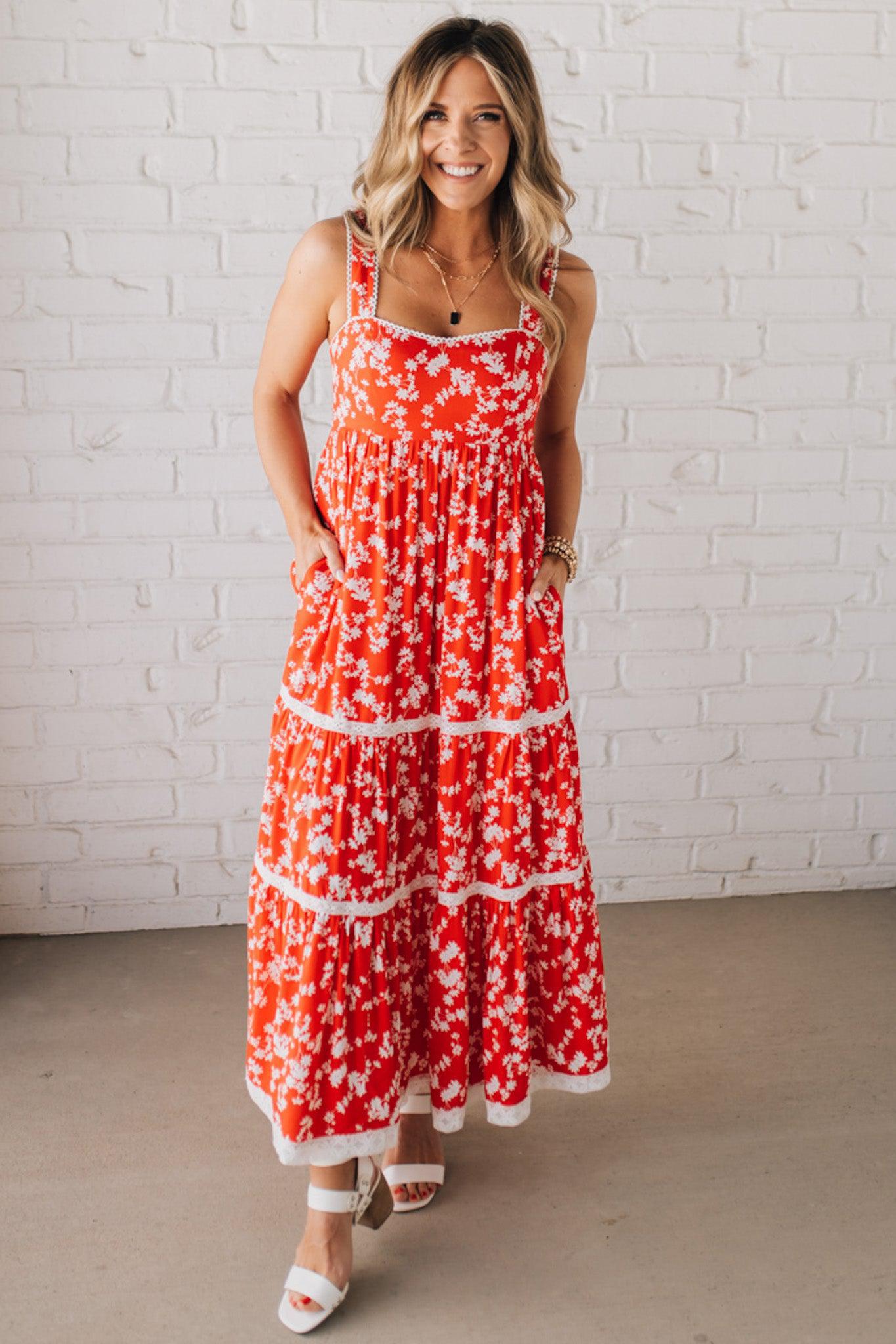 BLONDE WOMAN WEARING A RED FLORAL PRINT SLEEVELESS MAXI FEATURES: TIERED SKIRT PANEL WITH LACE INSET DETAIL, SMOCKED BACK, HIDDEN SIDE ZIPPER, THICK STRAPS WITH SCALLOPED LACE EDGES, SIDE POCKETS AND FULL LINING.