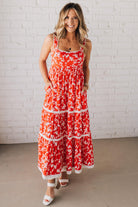 BLONDE WOMAN WEARING A RED FLORAL PRINT SLEEVELESS MAXI FEATURES: TIERED SKIRT PANEL WITH LACE INSET DETAIL, SMOCKED BACK, HIDDEN SIDE ZIPPER, THICK STRAPS WITH SCALLOPED LACE EDGES, SIDE POCKETS AND FULL LINING.