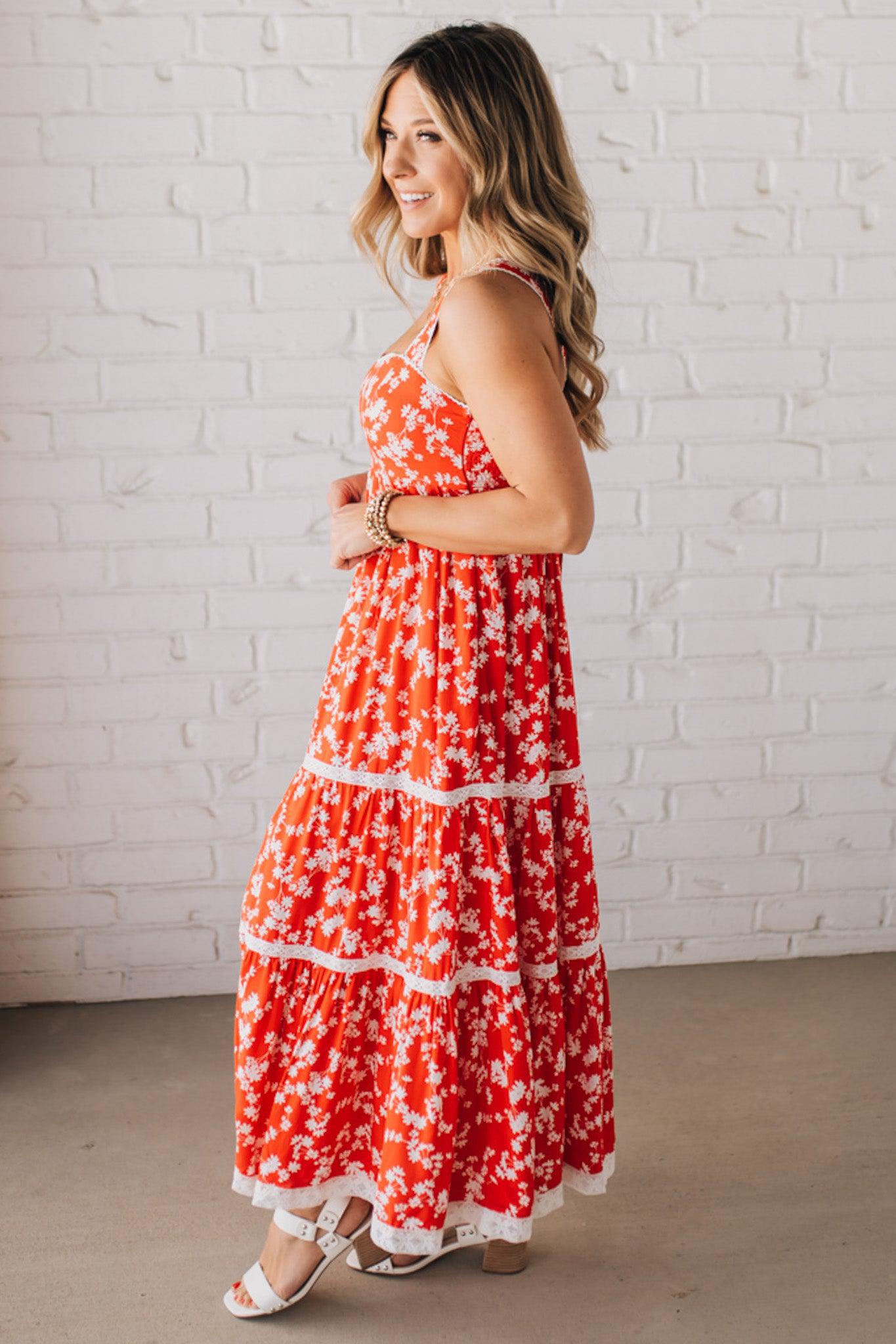 BLONDE WOMAN WEARING A RED FLORAL PRINT SLEEVELESS MAXI FEATURES: TIERED SKIRT PANEL WITH LACE INSET DETAIL, SMOCKED BACK, HIDDEN SIDE ZIPPER, THICK STRAPS WITH SCALLOPED LACE EDGES, SIDE POCKETS AND FULL LINING.