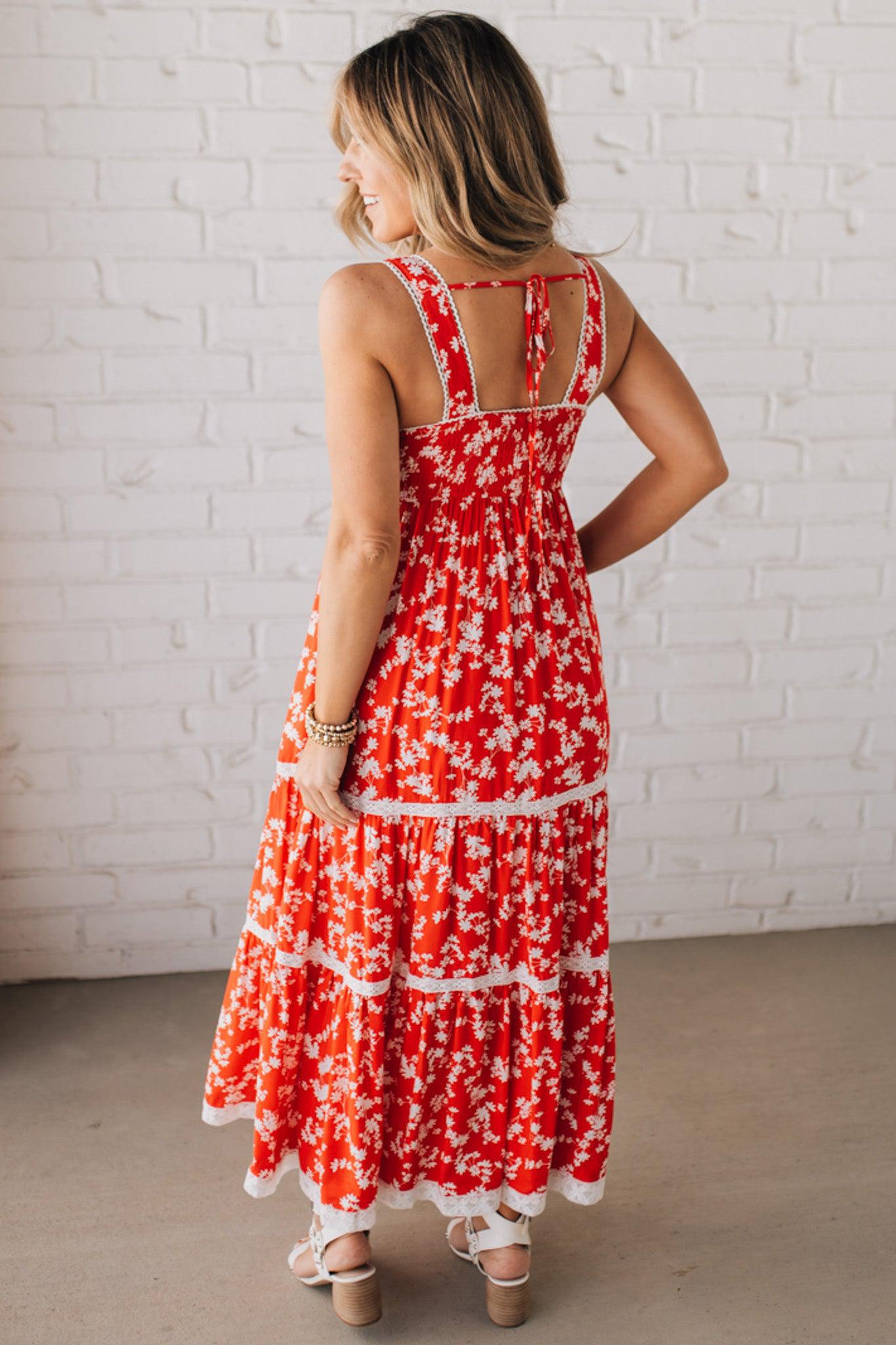 BLONDE WOMAN WEARING A RED FLORAL PRINT SLEEVELESS MAXI FEATURES: TIERED SKIRT PANEL WITH LACE INSET DETAIL, SMOCKED BACK, HIDDEN SIDE ZIPPER, THICK STRAPS WITH SCALLOPED LACE EDGES, SIDE POCKETS AND FULL LINING.