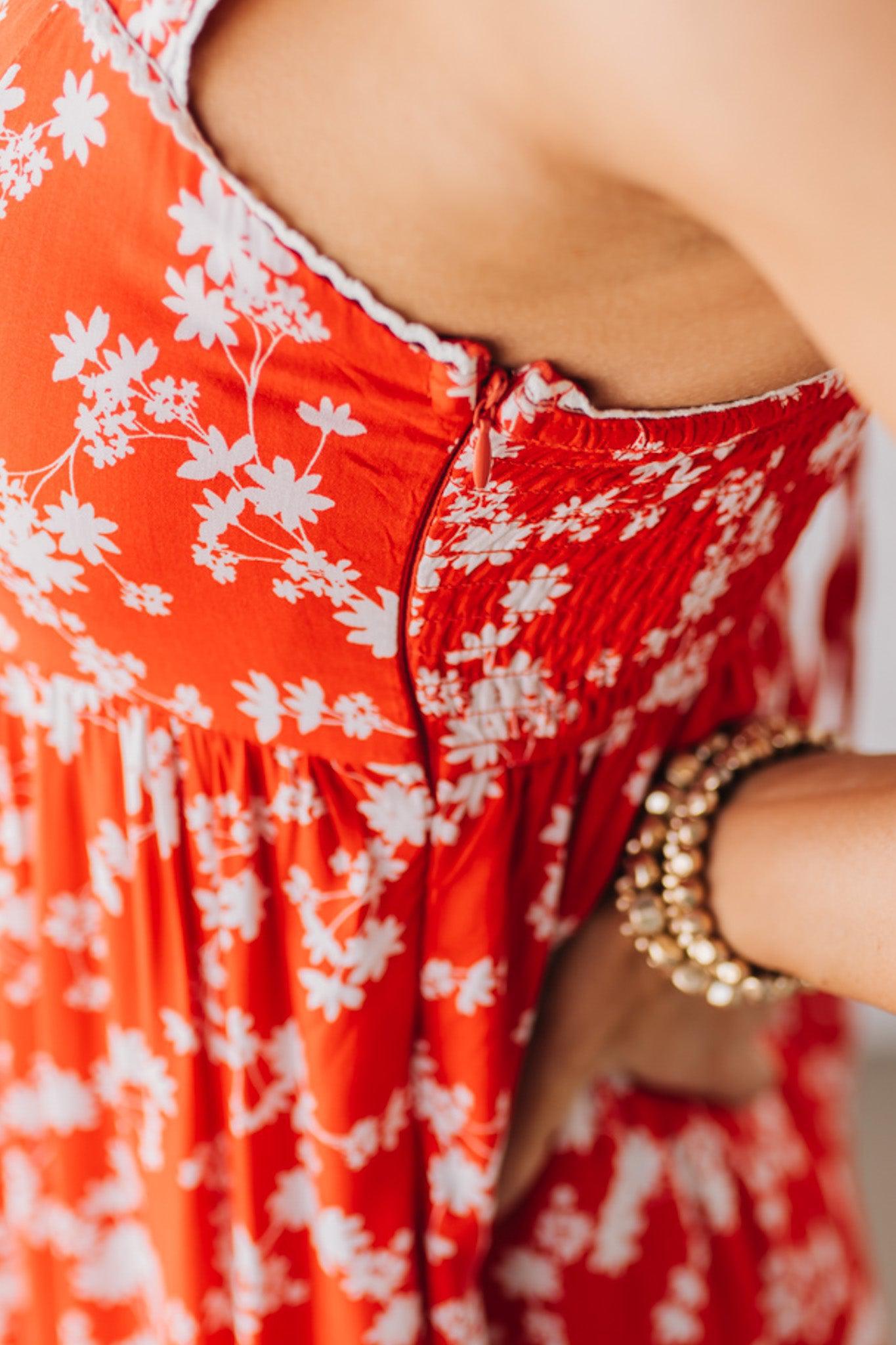 BLONDE WOMAN WEARING A RED FLORAL PRINT SLEEVELESS MAXI FEATURES: TIERED SKIRT PANEL WITH LACE INSET DETAIL, SMOCKED BACK, HIDDEN SIDE ZIPPER, THICK STRAPS WITH SCALLOPED LACE EDGES, SIDE POCKETS AND FULL LINING.