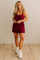Woman wearing a burgundy dress with white sneakers against a beige wall.