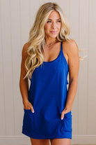 Blonde woman wearing a solid blue romper dress with side pockets.