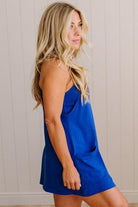 Blonde woman wearing a solid blue romper dress with side pockets.