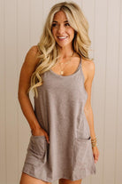 Woman wearing a gray sleeveless dress with pockets against a beige wall.