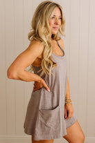 Woman wearing a gray dress with a pocket against a beige wall.