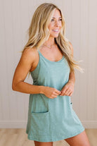 Blonde woman wearing a heathered teal green romper dress with side pockets.