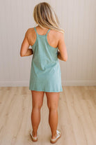Blonde woman wearing a heathered teal green romper dress with side pockets.