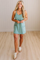 Blonde woman wearing a heathered teal green romper dress with side pockets.