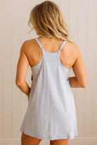 Woman wearing a light gray tank dress against a beige wall.