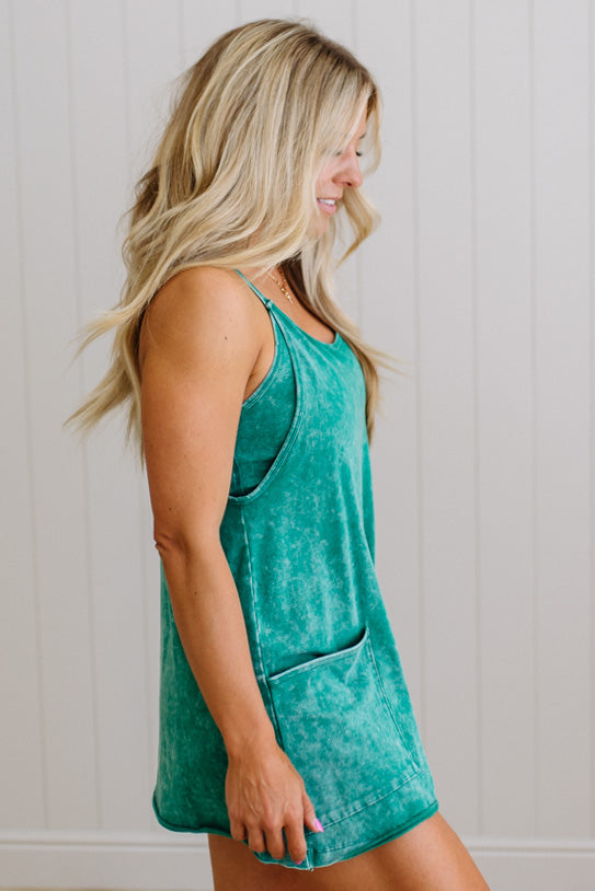 Woman wearing a teal sleeveless top with a pocket against a white wall.