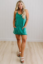 Woman wearing a green dress standing against a white paneled wall.
