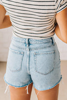 Woman wearing high-low distressed hem denim shorts light acid wash fringe edges.