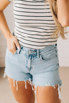 Woman wearing high-low distressed hem denim shorts light acid wash fringe edges.