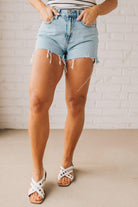 Woman wearing high-low distressed hem denim shorts light acid wash fringe edges.