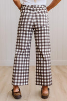 A person wearing brown and white gingham wide-leg cropped pants, paired with brown slide sandals and a white top, standing in a room with light wood floors and white paneled walls.
