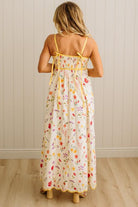 Woman wearing a floral dress with yellow straps against a white paneled wall.