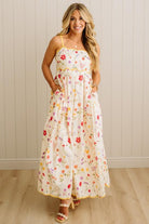 Woman wearing a floral dress standing against a light wooden paneled wall.