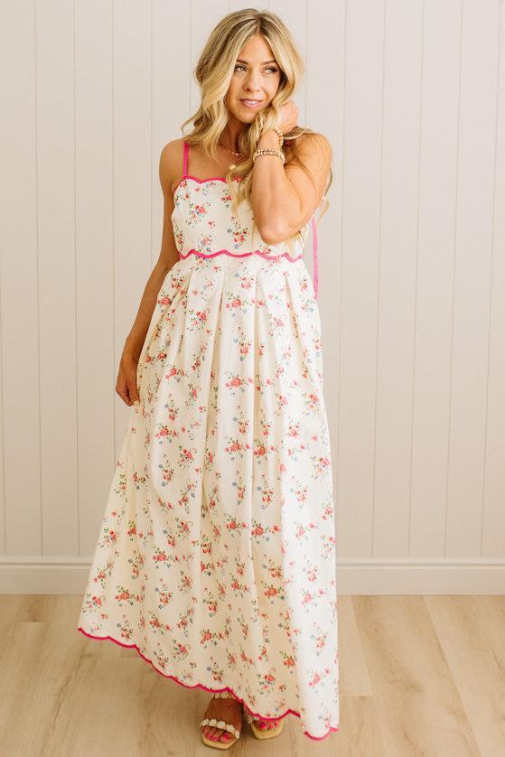 Woman wearing a floral dress with pink trim against a white paneled wall.