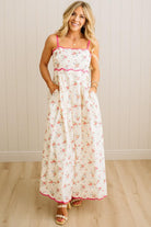 Woman wearing a floral dress with pink trim against a white paneled wall.