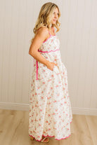 Woman wearing a floral dress with pink trim against a white paneled wall.