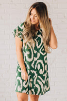 BLONDE WOMAN WEARING A GREEN AND CREAM ABSTRACT PRINTED FRILL SLEEVE SHIRT MINI DRESS.