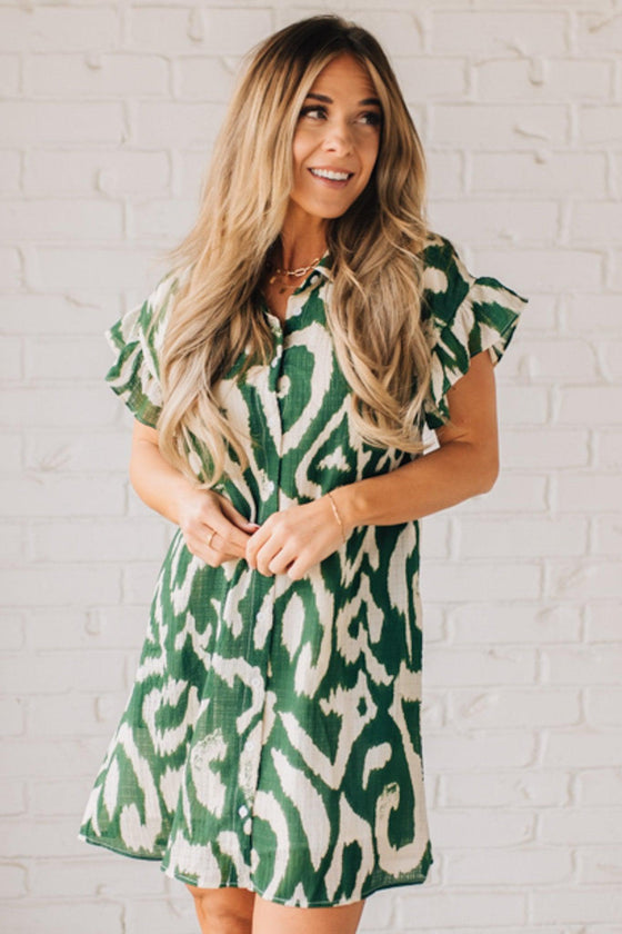 BLONDE WOMAN WEARING A GREEN AND CREAM ABSTRACT PRINTED FRILL SLEEVE SHIRT MINI DRESS.