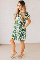 BLONDE WOMAN WEARING A GREEN AND CREAM ABSTRACT PRINTED FRILL SLEEVE SHIRT MINI DRESS.