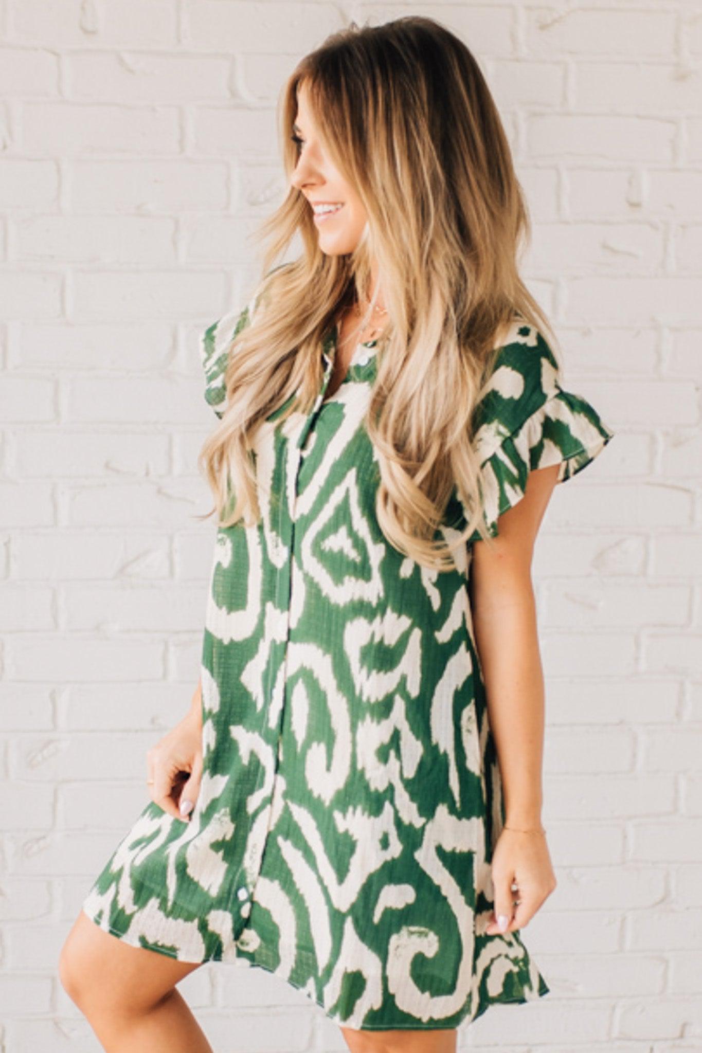 BLONDE WOMAN WEARING A GREEN AND CREAM ABSTRACT PRINTED FRILL SLEEVE SHIRT MINI DRESS.