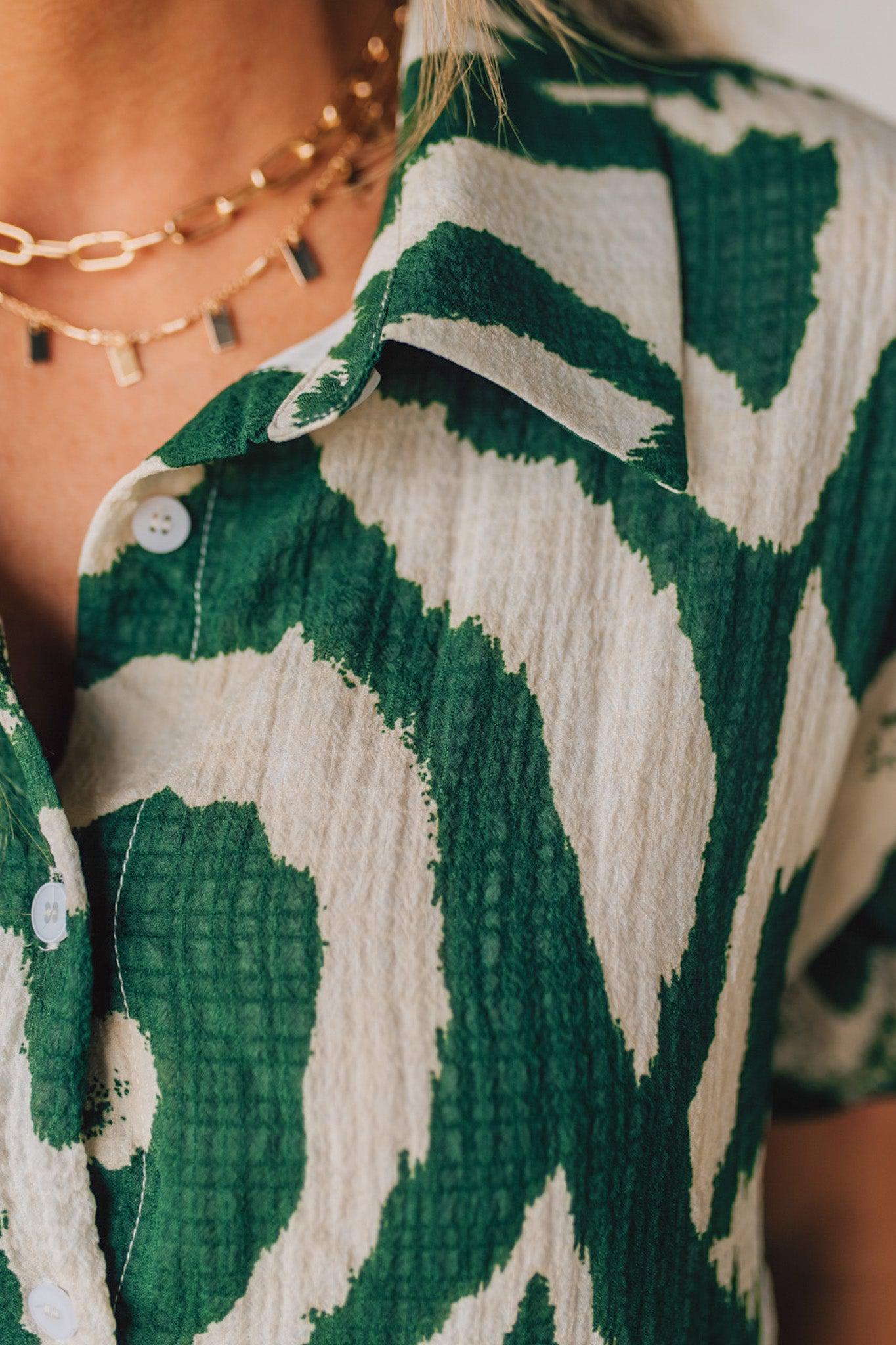 BLONDE WOMAN WEARING A GREEN AND CREAM ABSTRACT PRINTED FRILL SLEEVE SHIRT MINI DRESS.