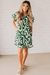 BLONDE WOMAN WEARING A GREEN AND CREAM ABSTRACT PRINTED FRILL SLEEVE SHIRT MINI DRESS.