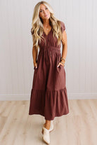 Blonde woman modeling a brown v-neck mid-length dress with tie front tassels and side pockets. 