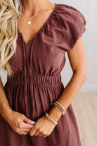 Blonde woman modeling a brown v-neck mid-length dress with tie front tassels and side pockets. 