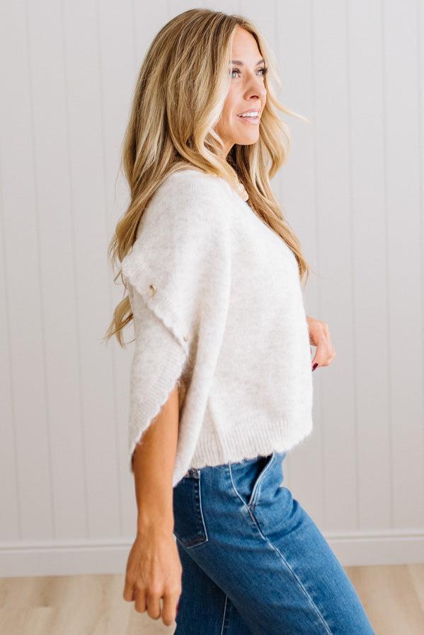BLONDE WOMAN WEARING DARK JEANS IN A BRIGHTLY LIT STUDIO WITH A SOLID SWEATER FEATURING SCALLOP TRIM AND BUTTONS UP THE SLEEVE IN THE COLOR HEATHERED OATMEAL.
